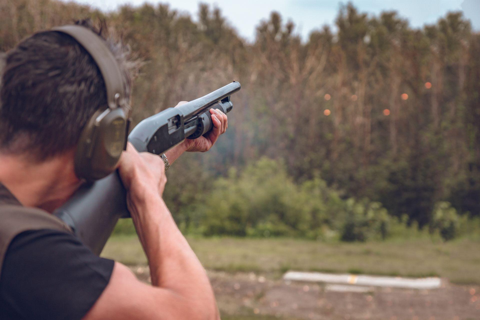 Ein Mann beim Schießtraining in der Natur. Er zielt mit einem Gewehr auf ein Ziel im Wald, während die Sonne durch die Bäume scheint.