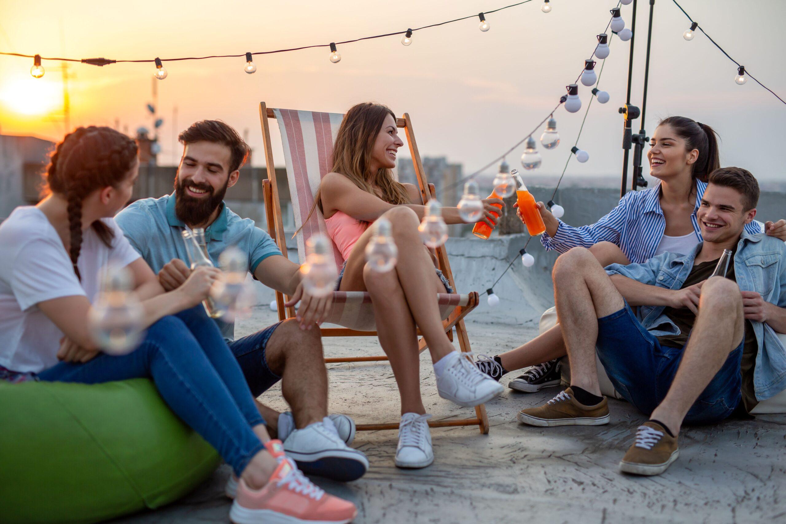 Gruppe junger Menschen entspannt sich auf einer begrünten Dachterrasse mit Lichterketten