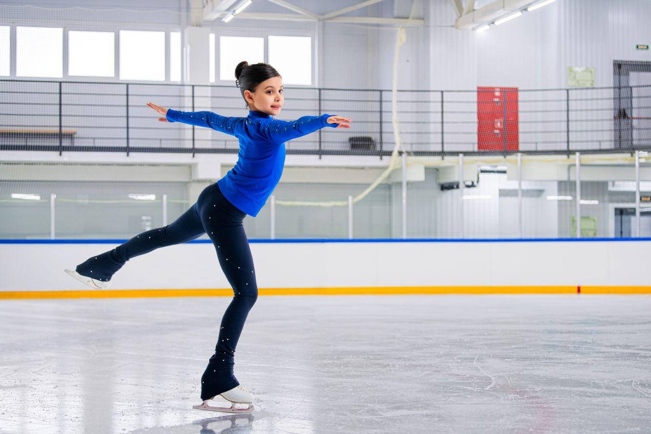 Maedchen in blauer Kleidung beim Eiskunstlauf – elegante Bewegung auf Eis mit Bauer Schlittschuhen in professioneller Umgebung