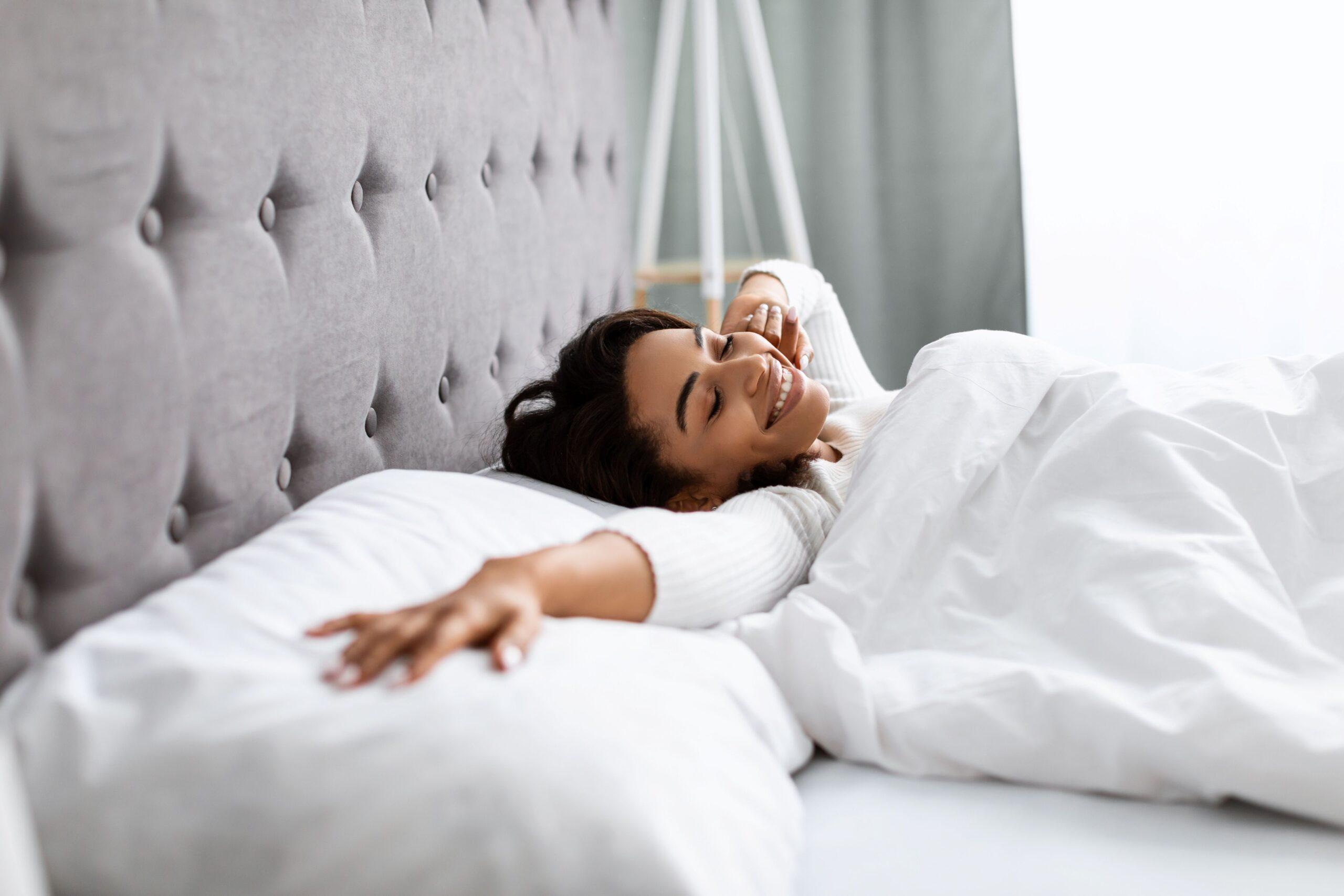 Junge Frau streckt sich morgens entspannt im Bett – Symbolbild für erholsamen Schlaf und mehr Wohlbefinden durch Griffonia