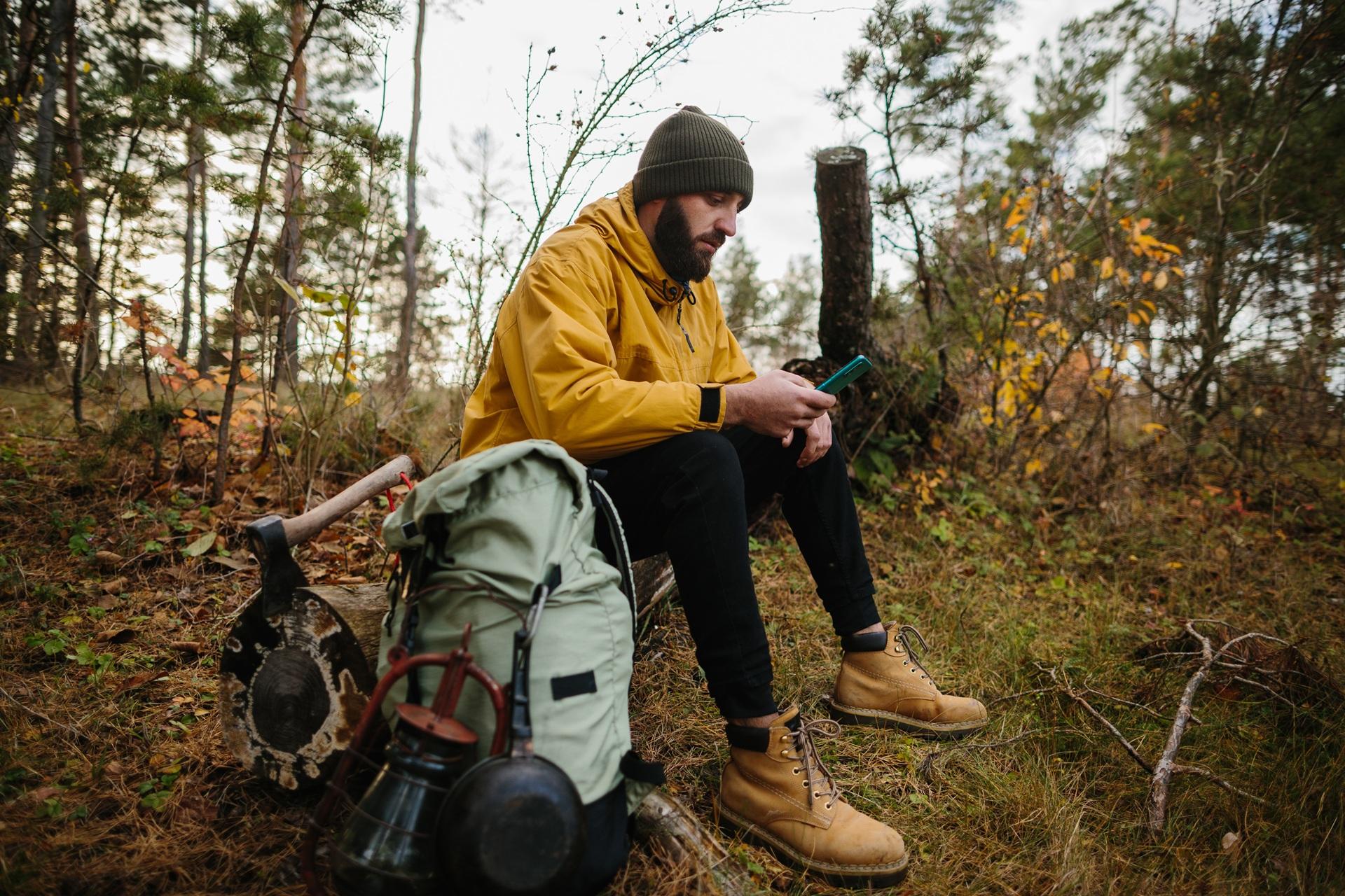 Mann mit Rucksack macht Pause im Wald und schaut aufs Handy | Vuse go